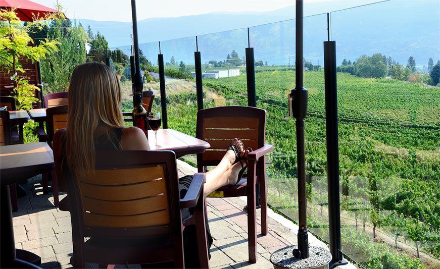 A woman is sitting at a table with her feet up in front of a vineyard.
