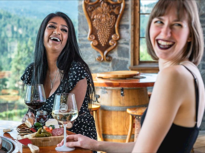 Two women are sitting at a table drinking wine and laughing.