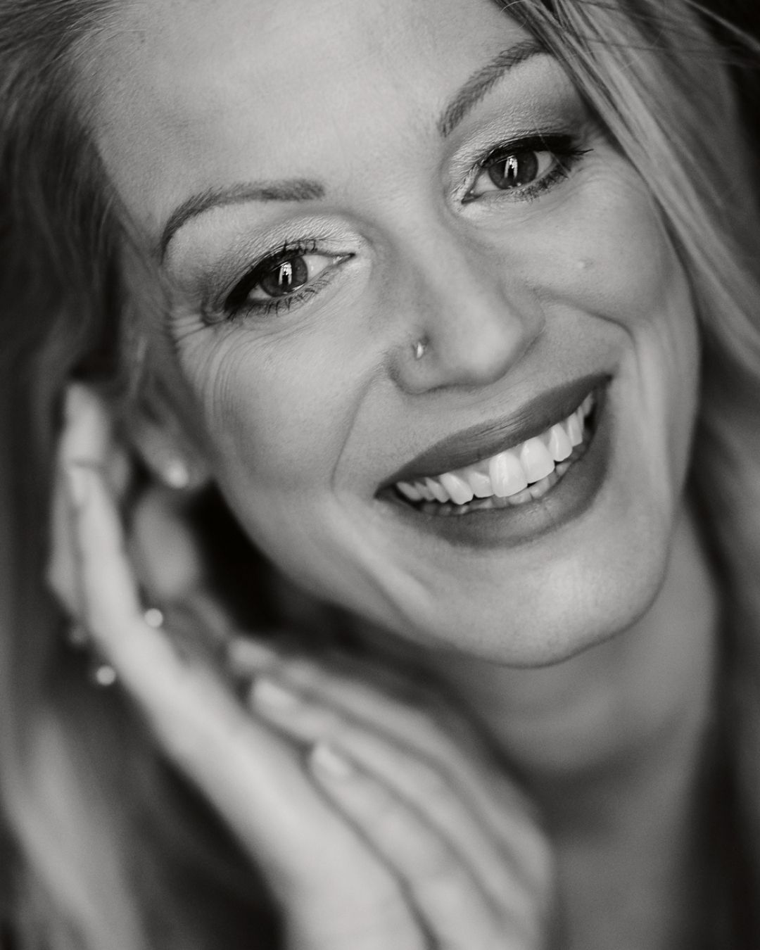Ein Schwarzweissfoto einer lächelnden Frau mit der Hand im Gesicht.