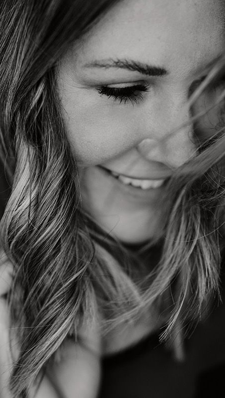 Ein Schwarzweissfoto einer lächelnden Frau, deren Haare im Wind wehen.