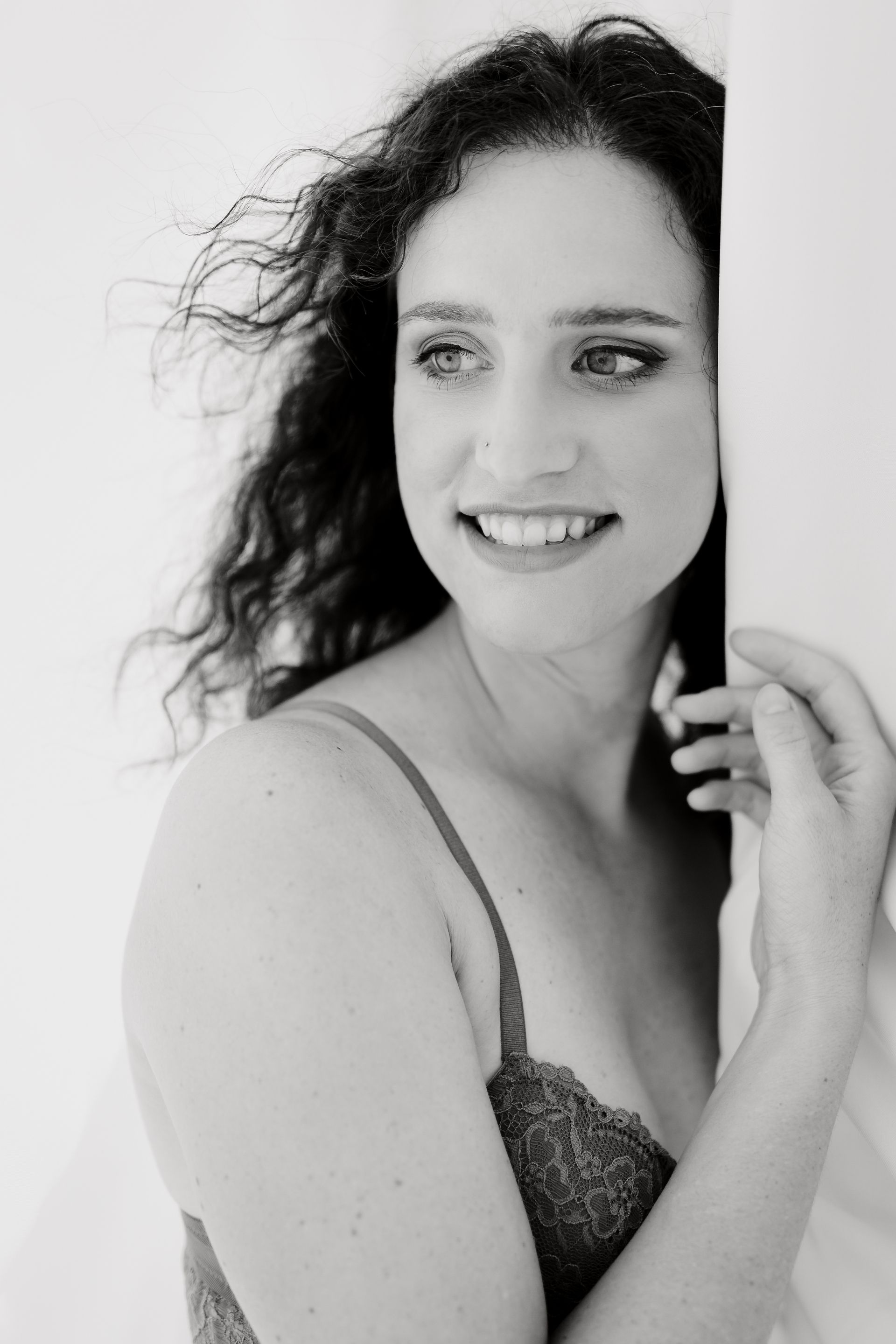 Ein Schwarzweissfoto einer Frau in Dessous, die hinter einer Wand hervorschaut.