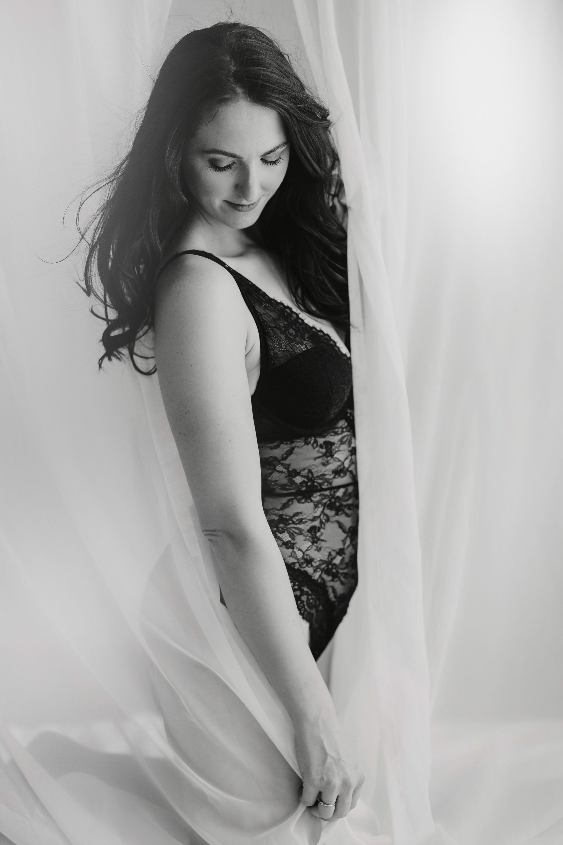 Eine Frau in Dessous kniet vor einem weissen Vorhang.