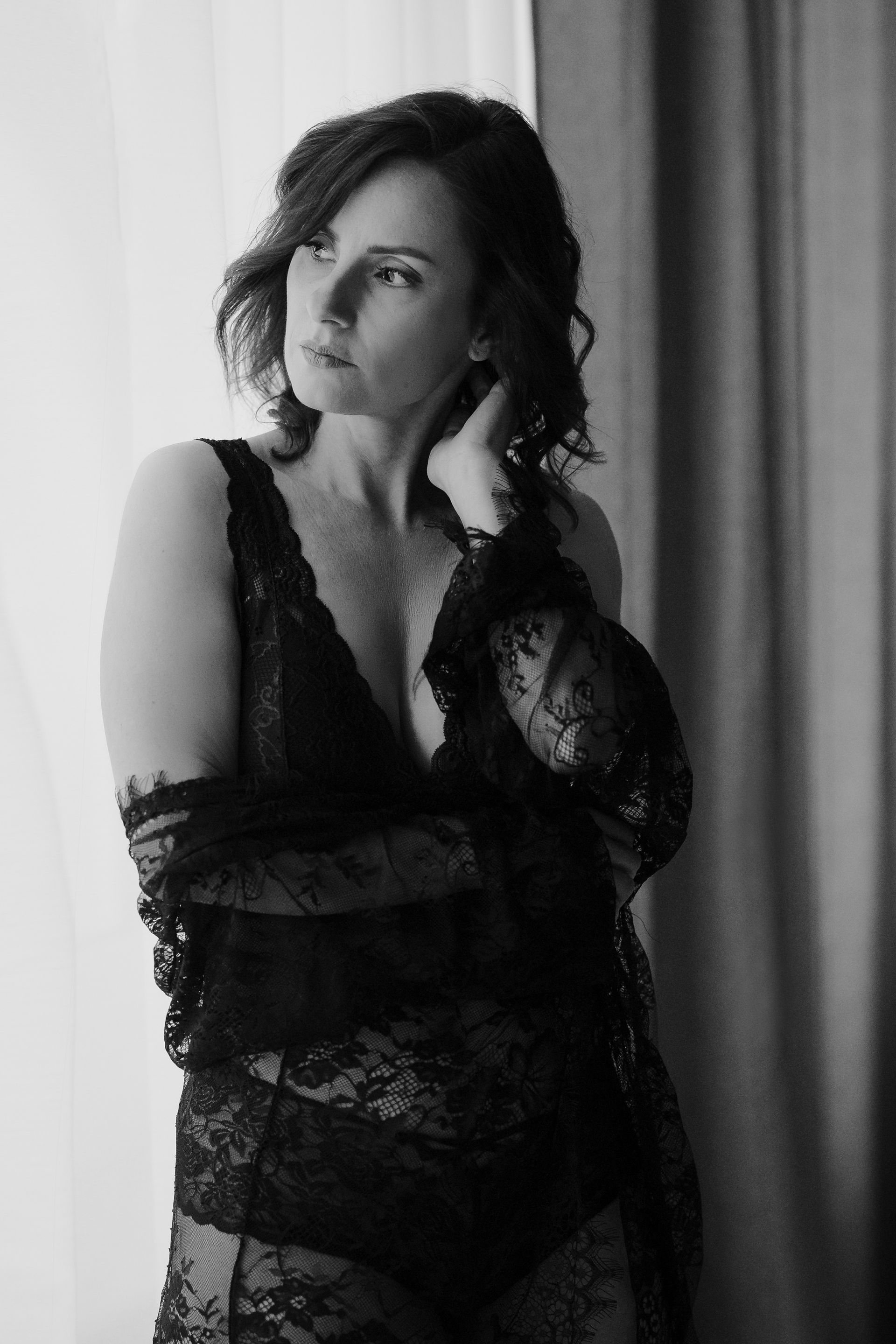 Eine Frau in einem schwarzen Spitzenbody steht vor einem Fenster.