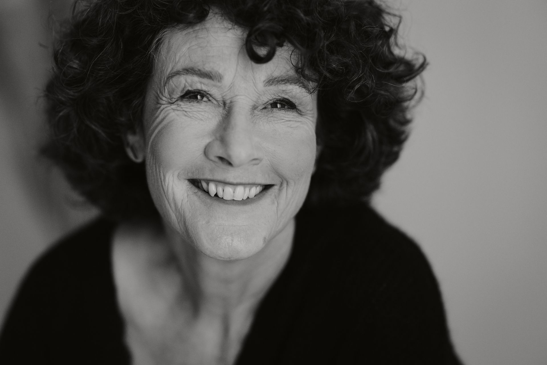 Eine Frau mit lockigem Haar lächelt auf einem Schwarzweissfoto.
