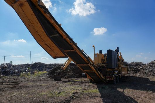 Yellow front-end loader in a sand pit. Tan and brown mounds of dirt and trees in the background.