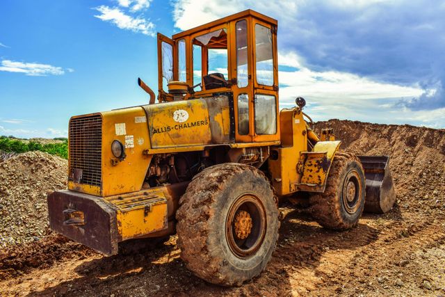 Yellow construction loader on a dirt pile under a partly cloudy blue sky.