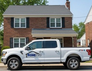 A white pickup truck with the HomePro logo parked in front of a two-story brick house with a gray shingle roof.