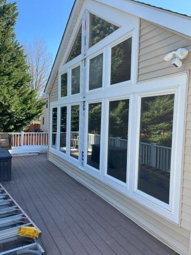 A tan house with a large grid of white-framed windows overlooks a wooden deck on a sunny day.