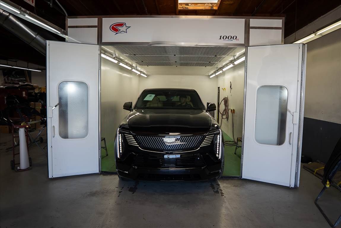 Black car inside a white paint booth, doors open.
