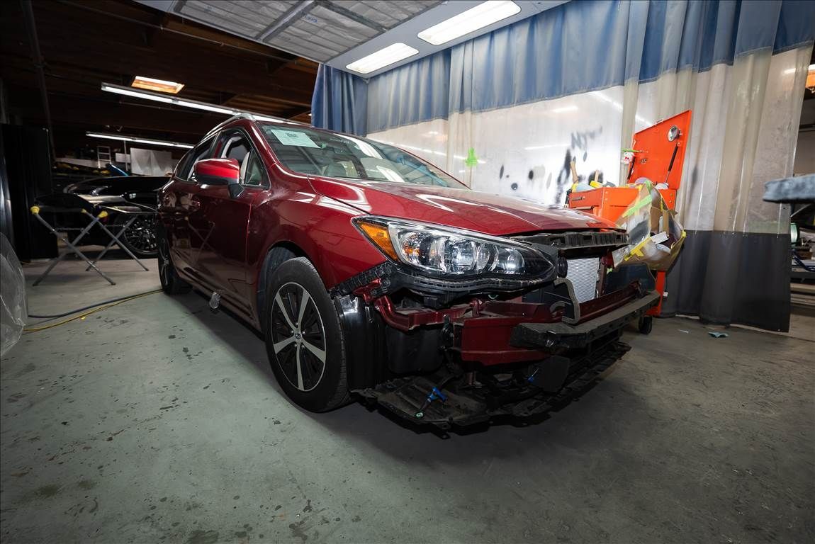 Damaged red car in a repair shop, front end collision visible.
