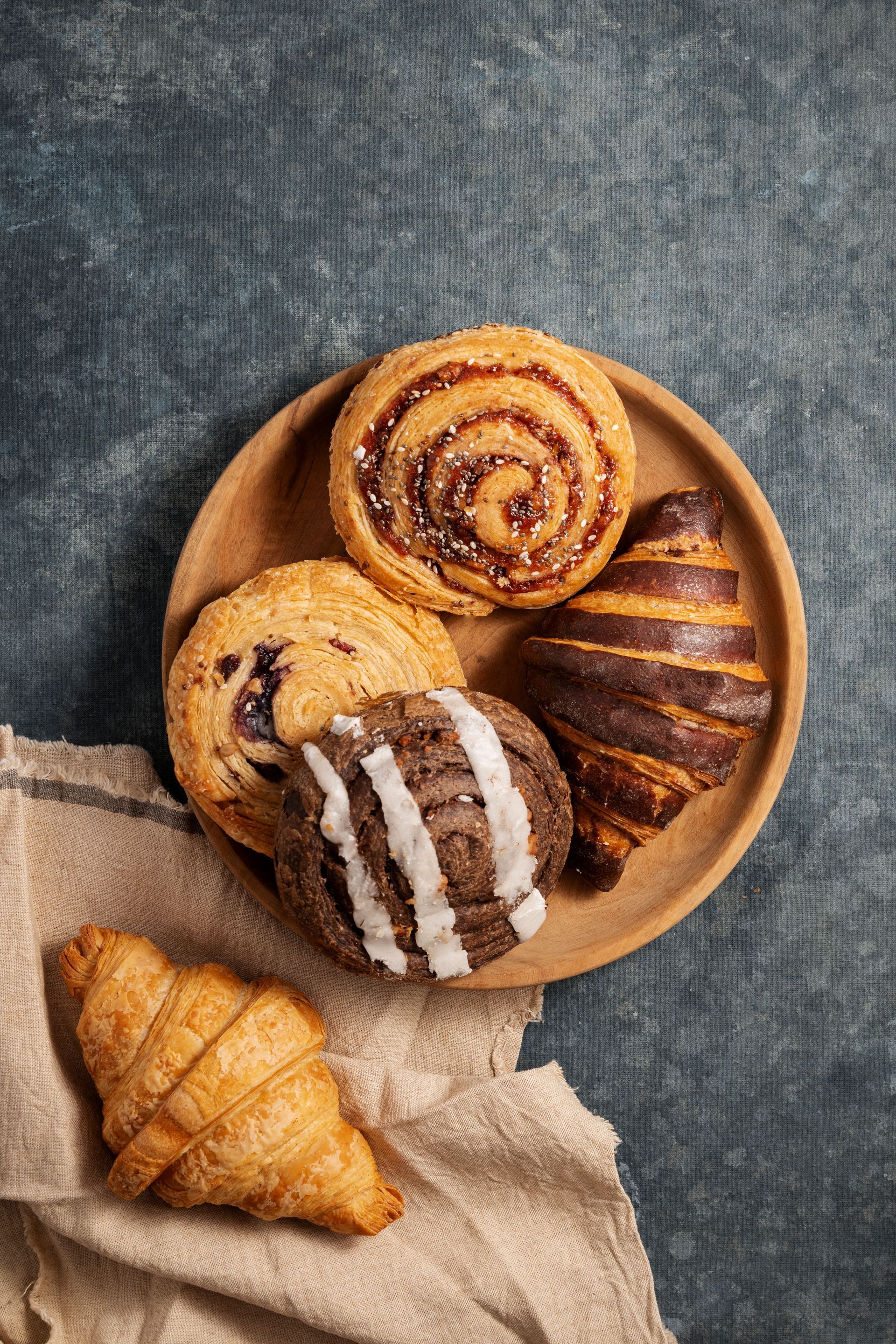 A wooden plate topped with a variety of pastries and croissants.