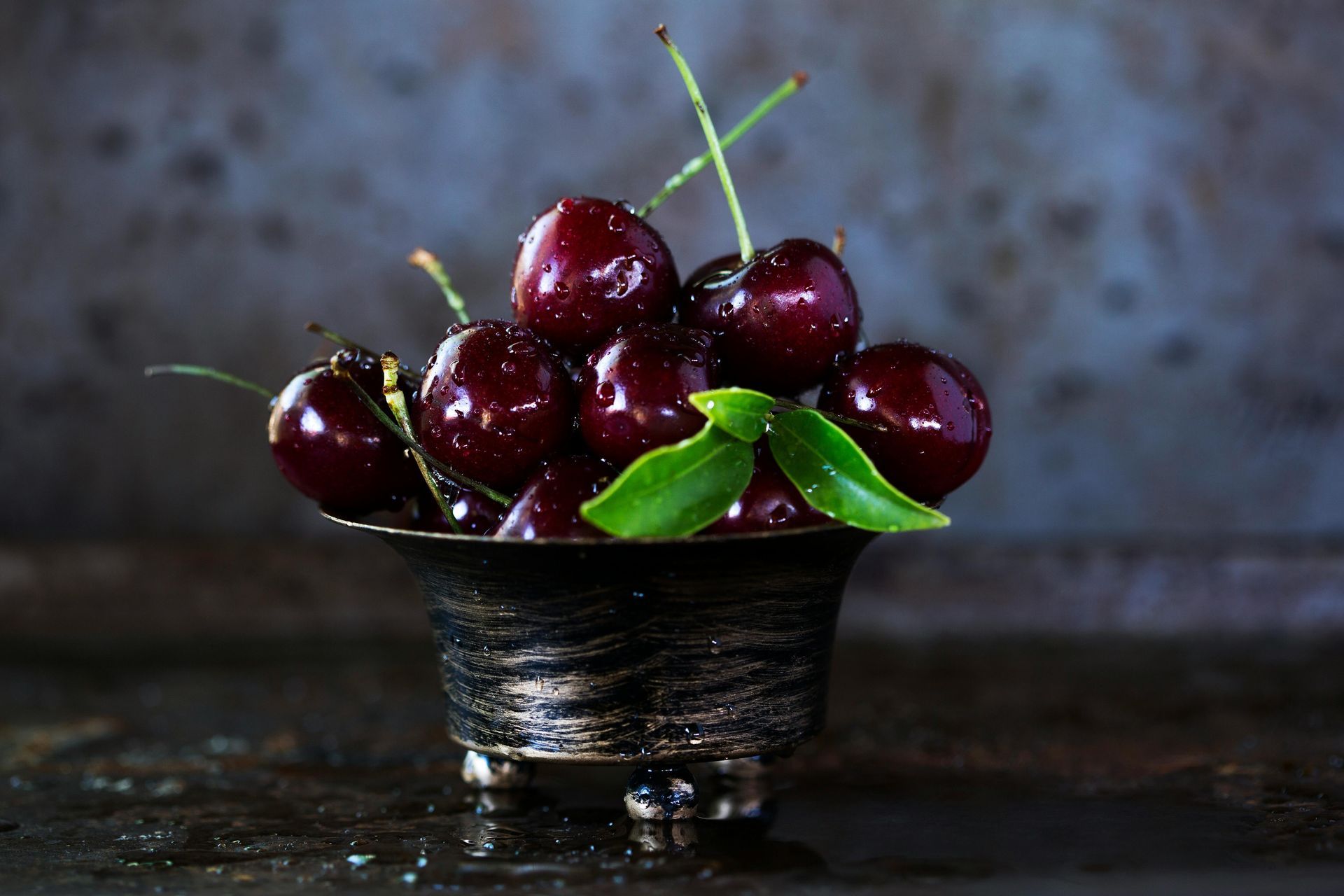A bowl of cherries with green leaves on a table.