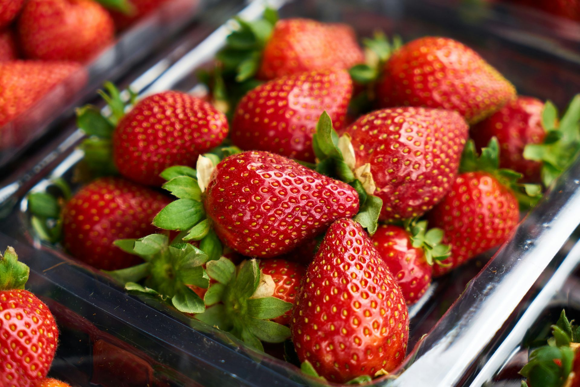 A plastic container filled with strawberries and green leaves.