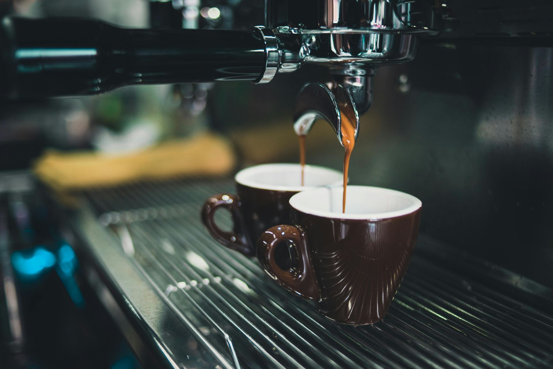 Two cups of coffee are being poured into a coffee machine.