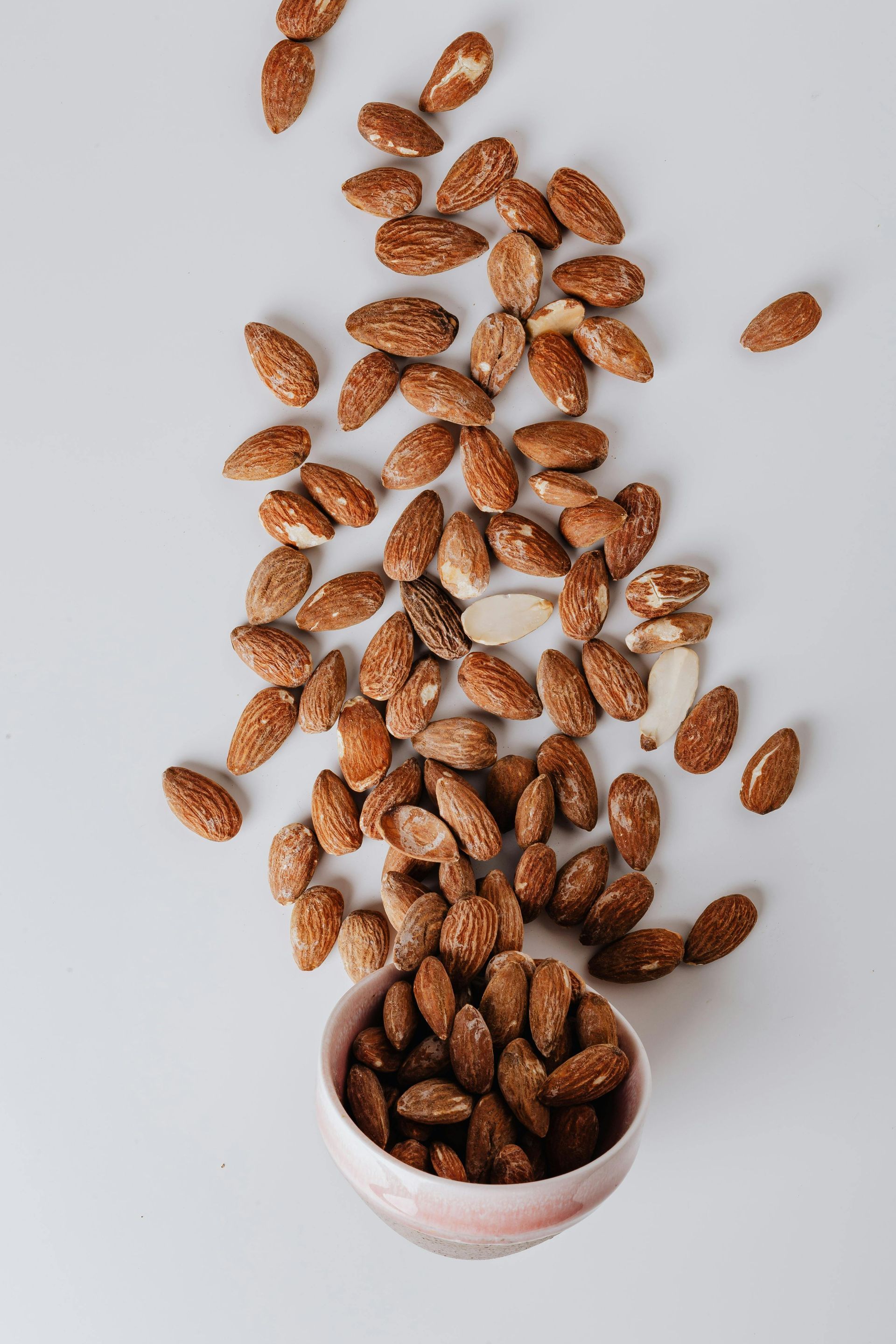 A bowl of almonds is sitting on a table next to a pile of almonds.