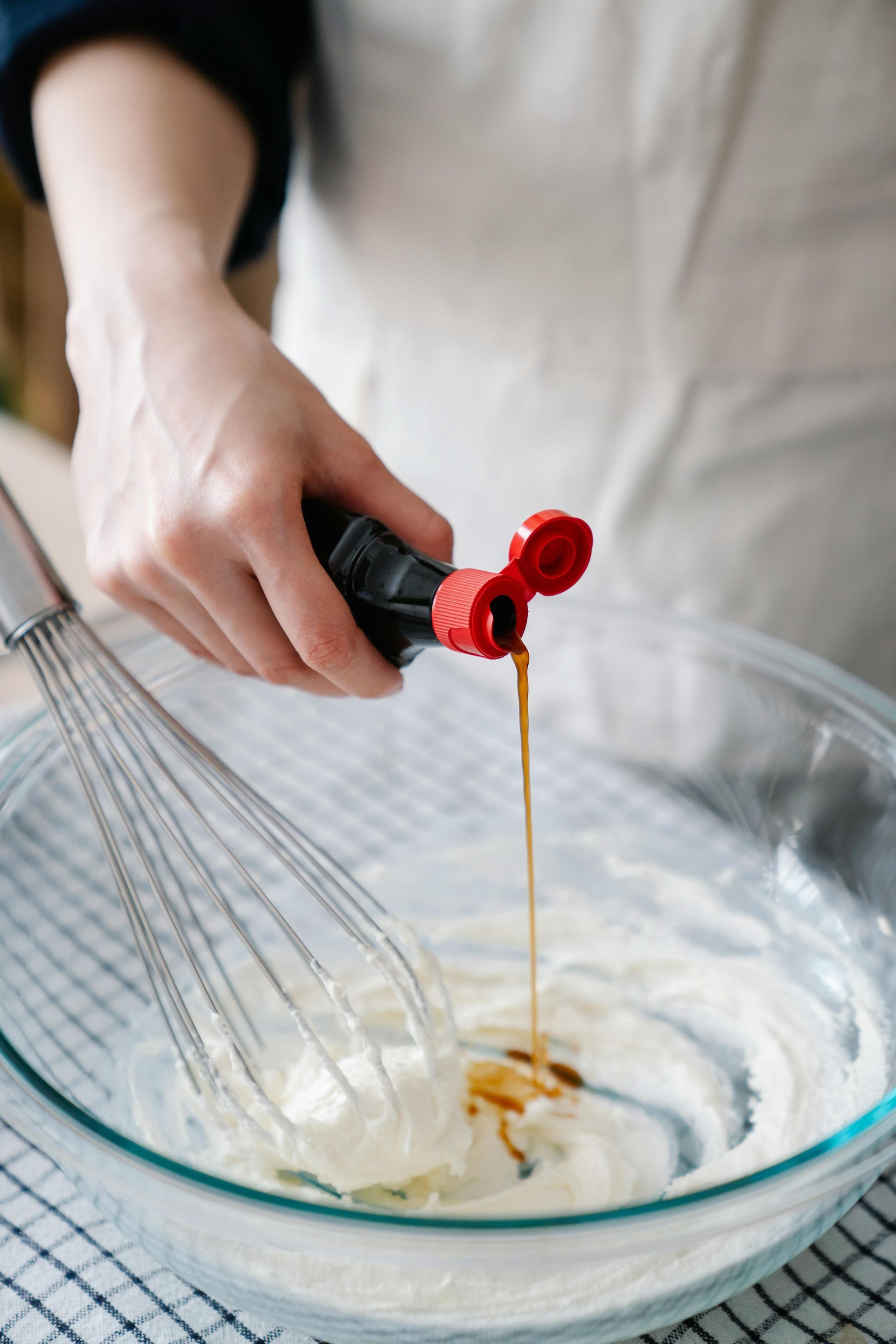A person is pouring syrup into a glass bowl with a whisk.