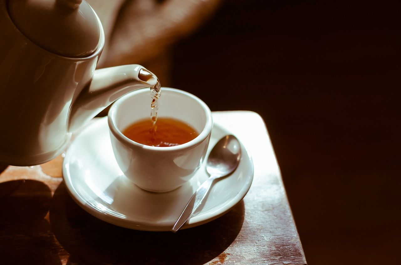 A cup of tea is being poured from a teapot into a cup on a saucer.