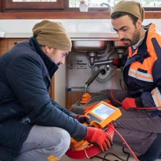 Two San Clemente Plumbers are working on a drain pipe under a sink