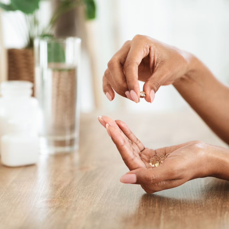 Eine Frau nimmt auf einem Holztisch eine Pille aus ihrer Hand.