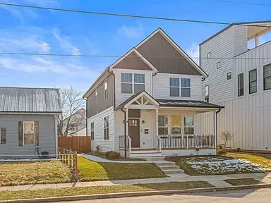 Two-story white house with brown accents, porch, and a small yard on a sunny day.