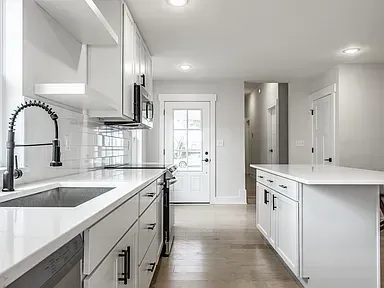 Bright white kitchen with stainless steel appliances, black faucet, and island.