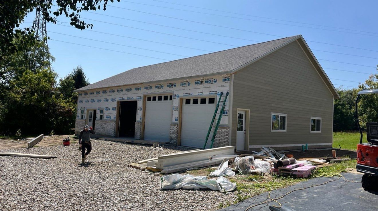 Garage under construction with two garage doors, beige siding, and a person walking. Garage under construction with two garage doors, beige siding, and a person walking.