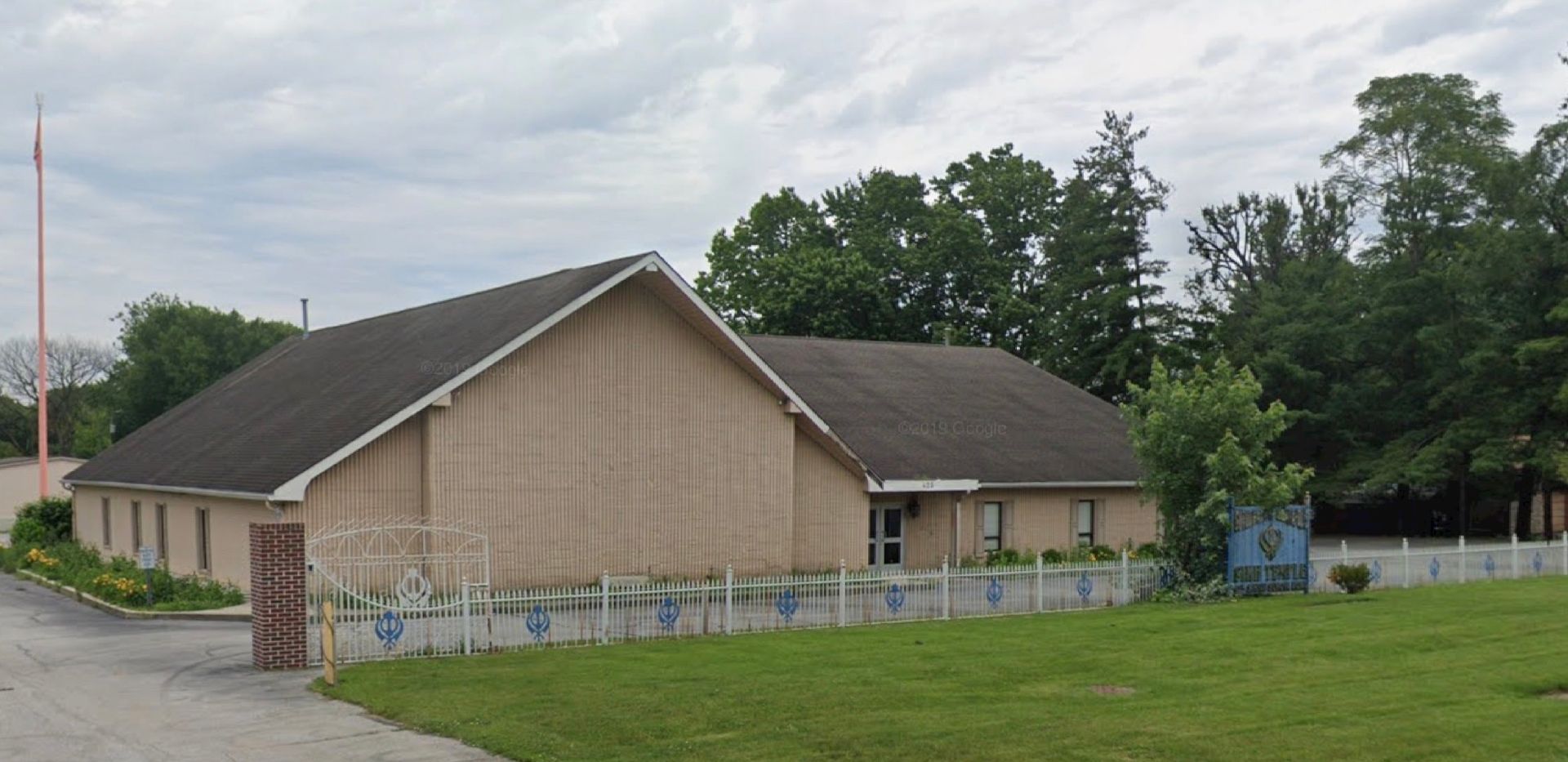 A beige building with a dark roof and a white picket fence on a cloudy day.