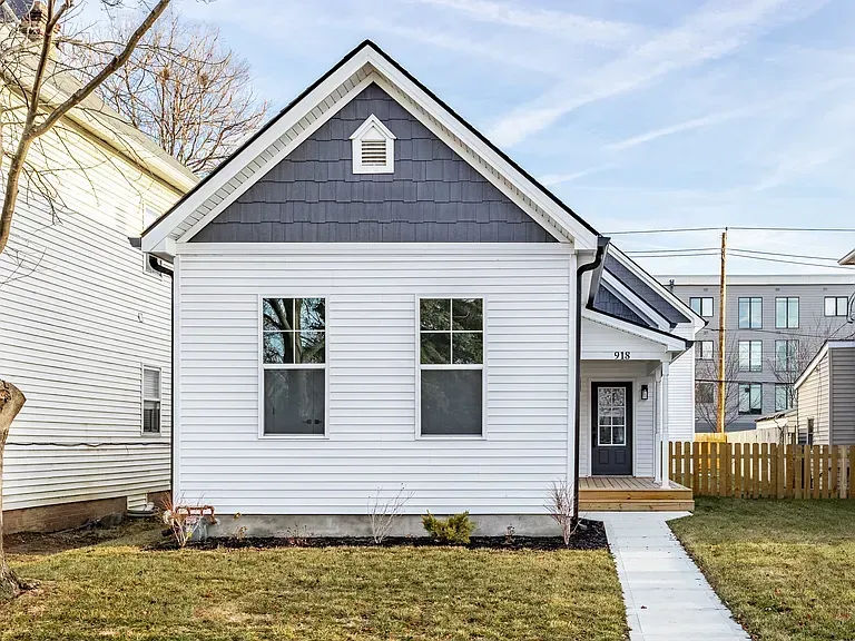 Two-story house frame under construction in snowy field, next to existing homes.