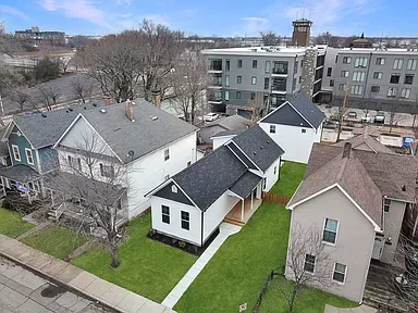 Aerial view of several houses with dark roofs and green lawns in a city neighborhood.