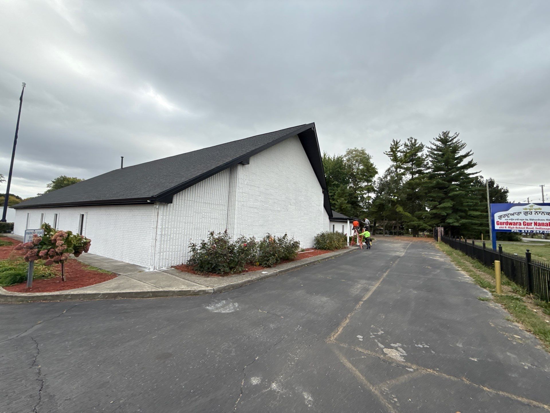 A beige building with a dark roof and a white picket fence on a cloudy day.