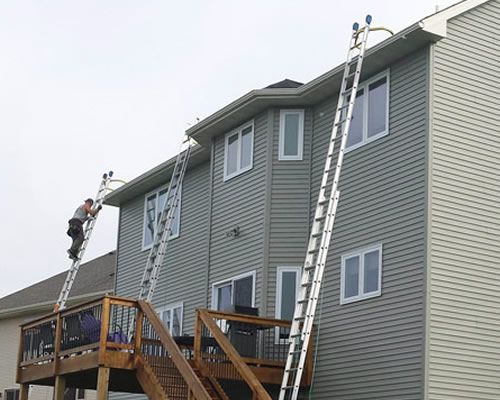 A man is standing on a ladder on the side of a house.