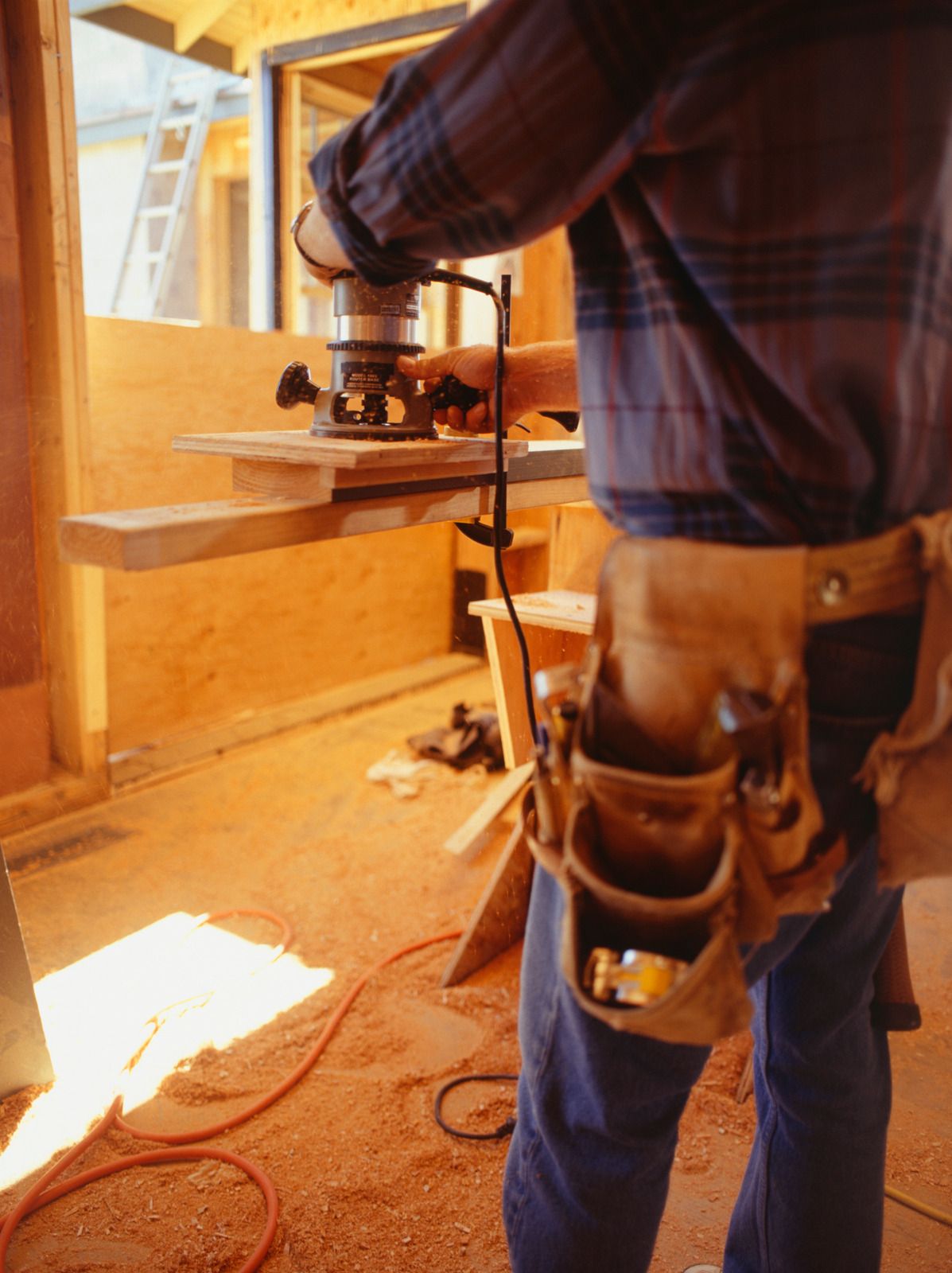 Carpenter using a router on a wooden board at a construction site.