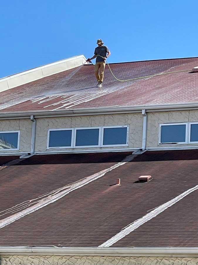 A man is spraying water on the roof of a building.