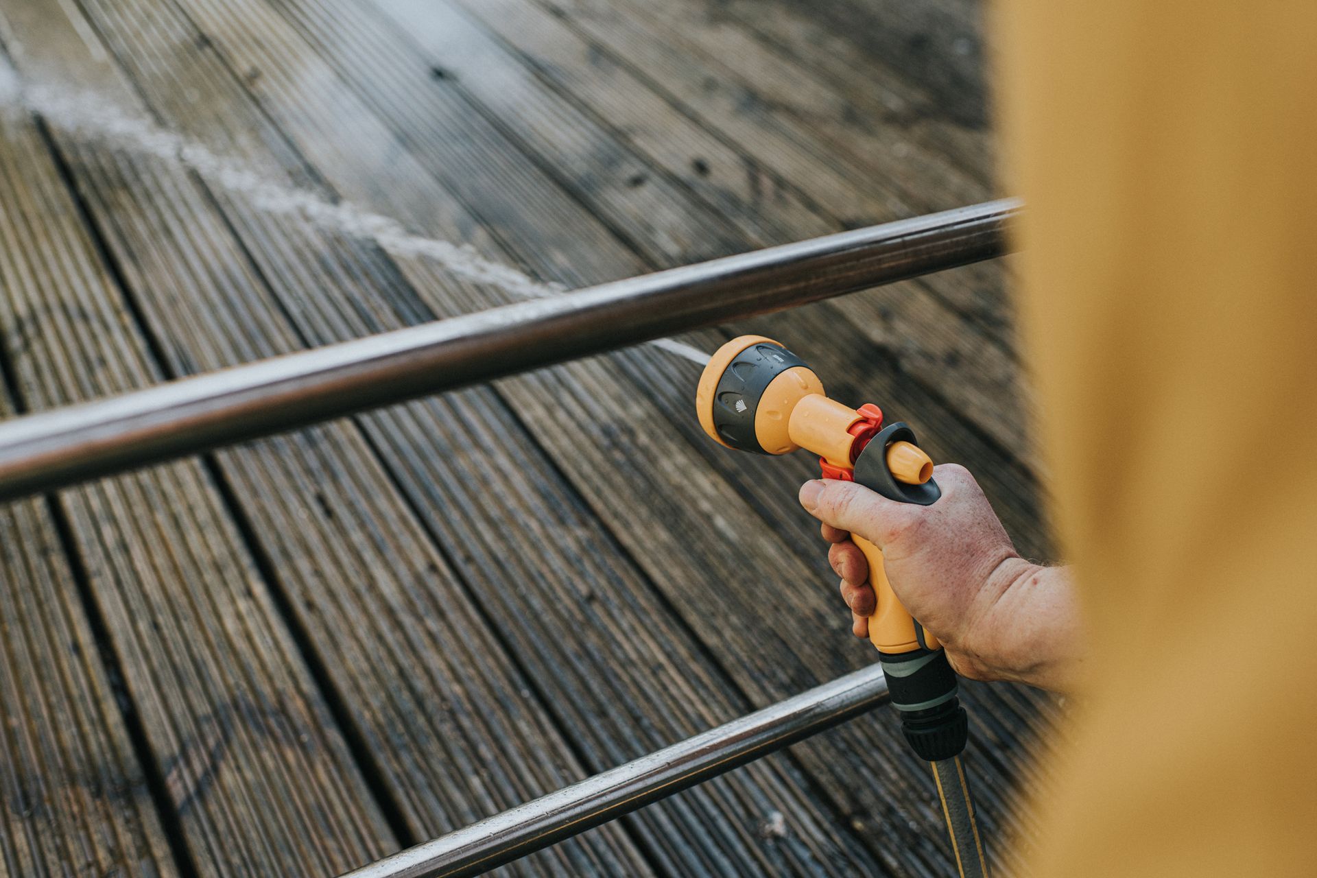  Residential pressure washing of wooden deck using spray nozzle held by person in yellow jacket.