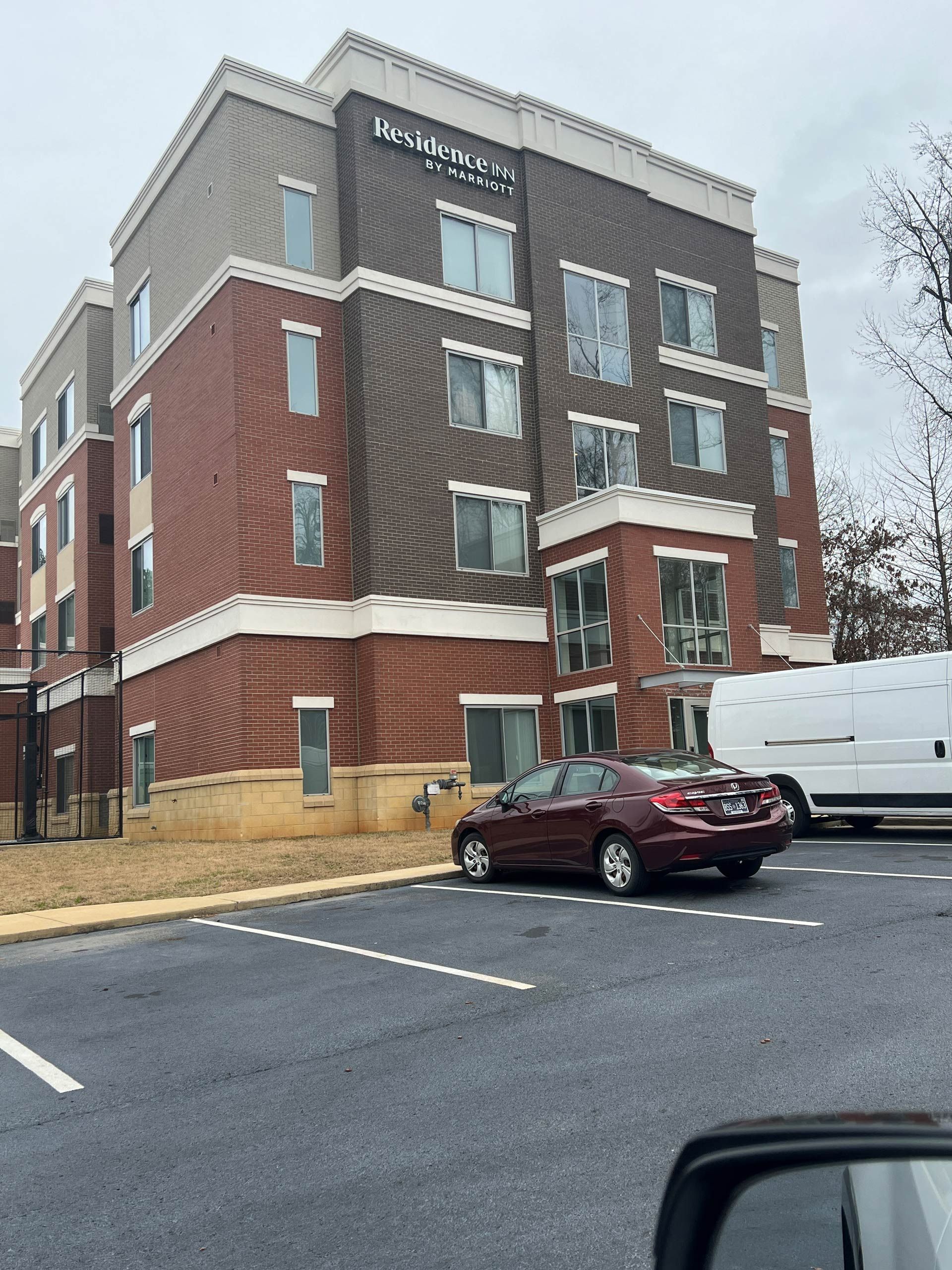 A red car is parked in front of a large brick building.