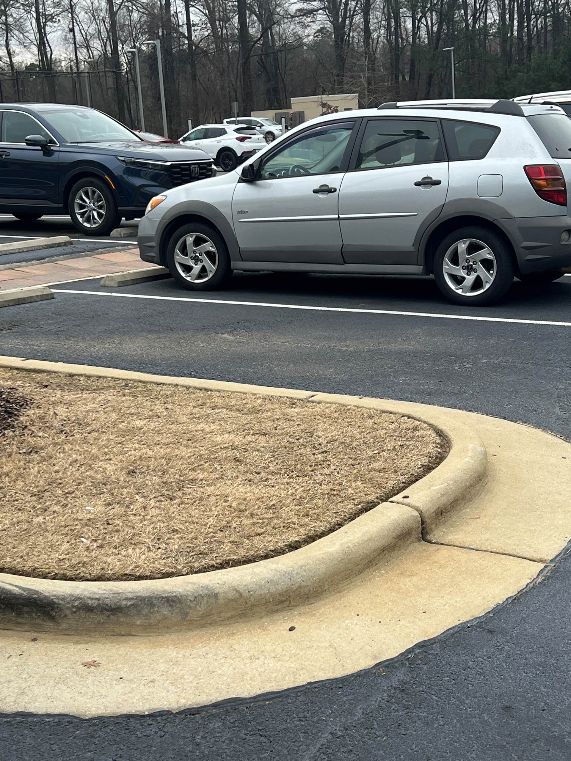 A silver car is parked in a parking lot next to a curb.