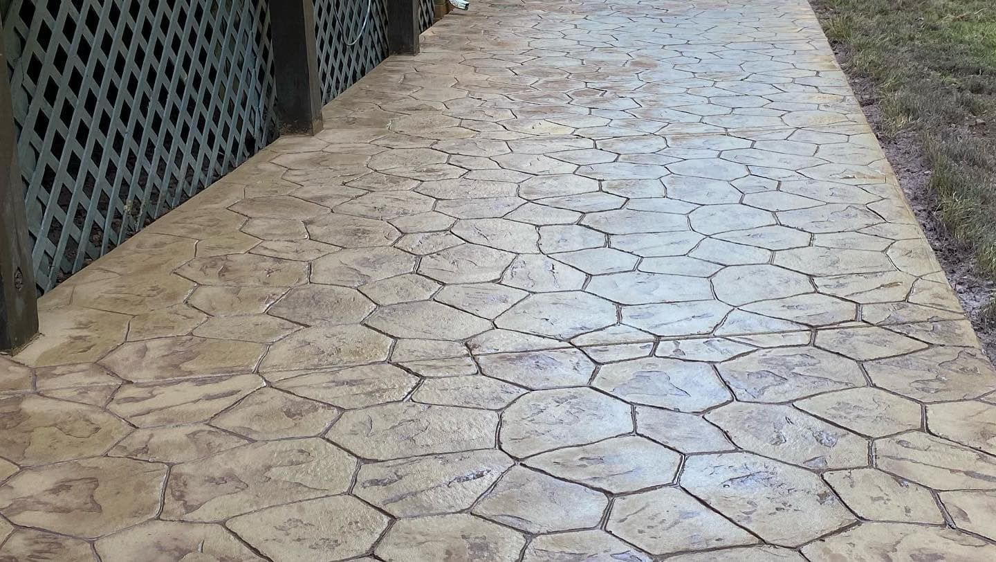 Stamped concrete walkway with irregular stone pattern, bordered by a lattice fence.