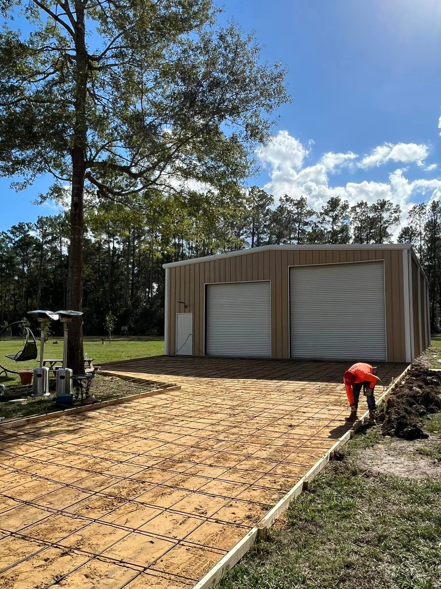 A construction site: a garage-like building with two bays, a driveway in progress, and a worker in orange.