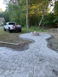 A white pickup truck parked near a newly constructed stone patio with a fire pit in a backyard setting.