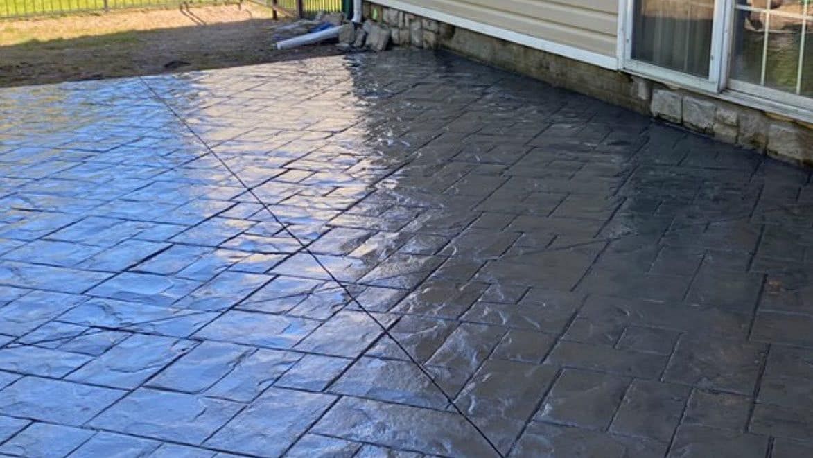 Stamped concrete patio with a dark gray, stone-like pattern next to a house.