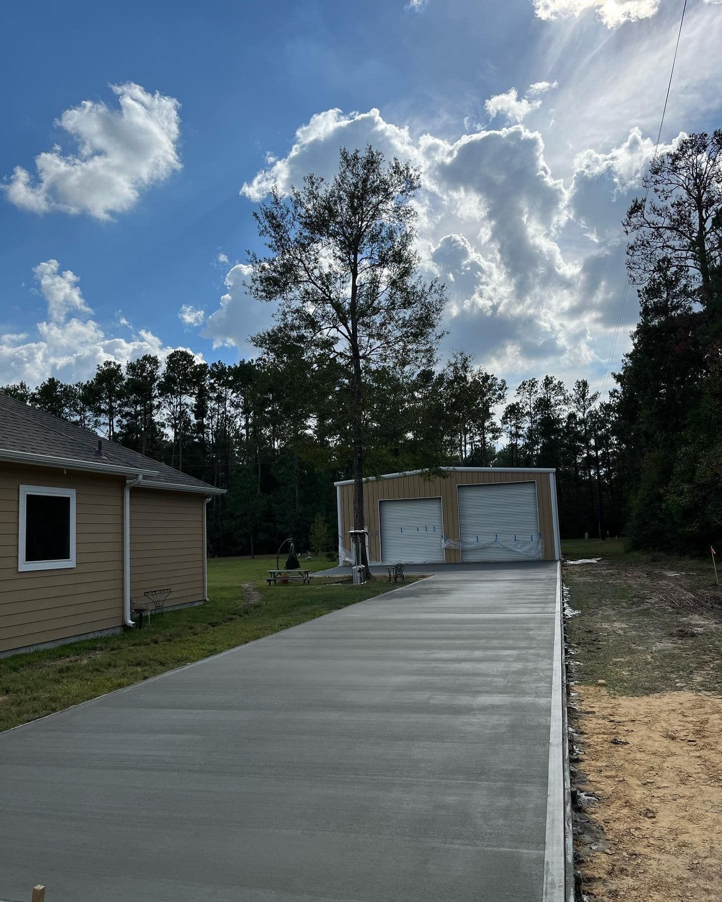 New concrete driveway leading to a garage with closed doors under a cloudy blue sky.