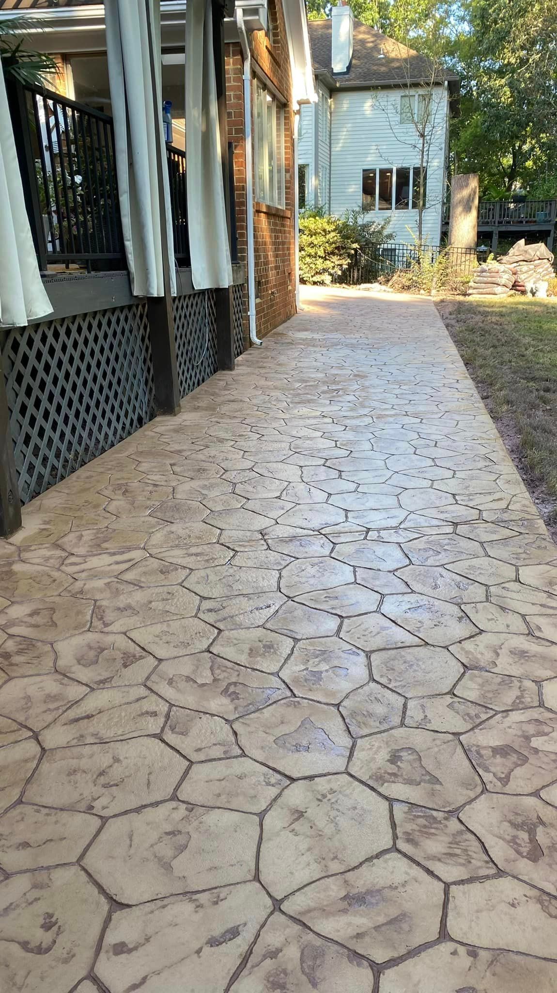A stone-patterned walkway alongside a building with a porch. Warm tan and brown colors.