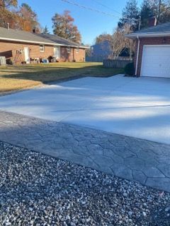 Newly paved driveway with patterned edge, next to a house and gravel.