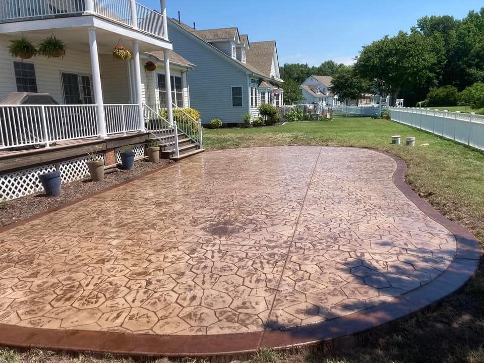 Stamped concrete patio next to a house with a brown border and design, surrounded by grass.