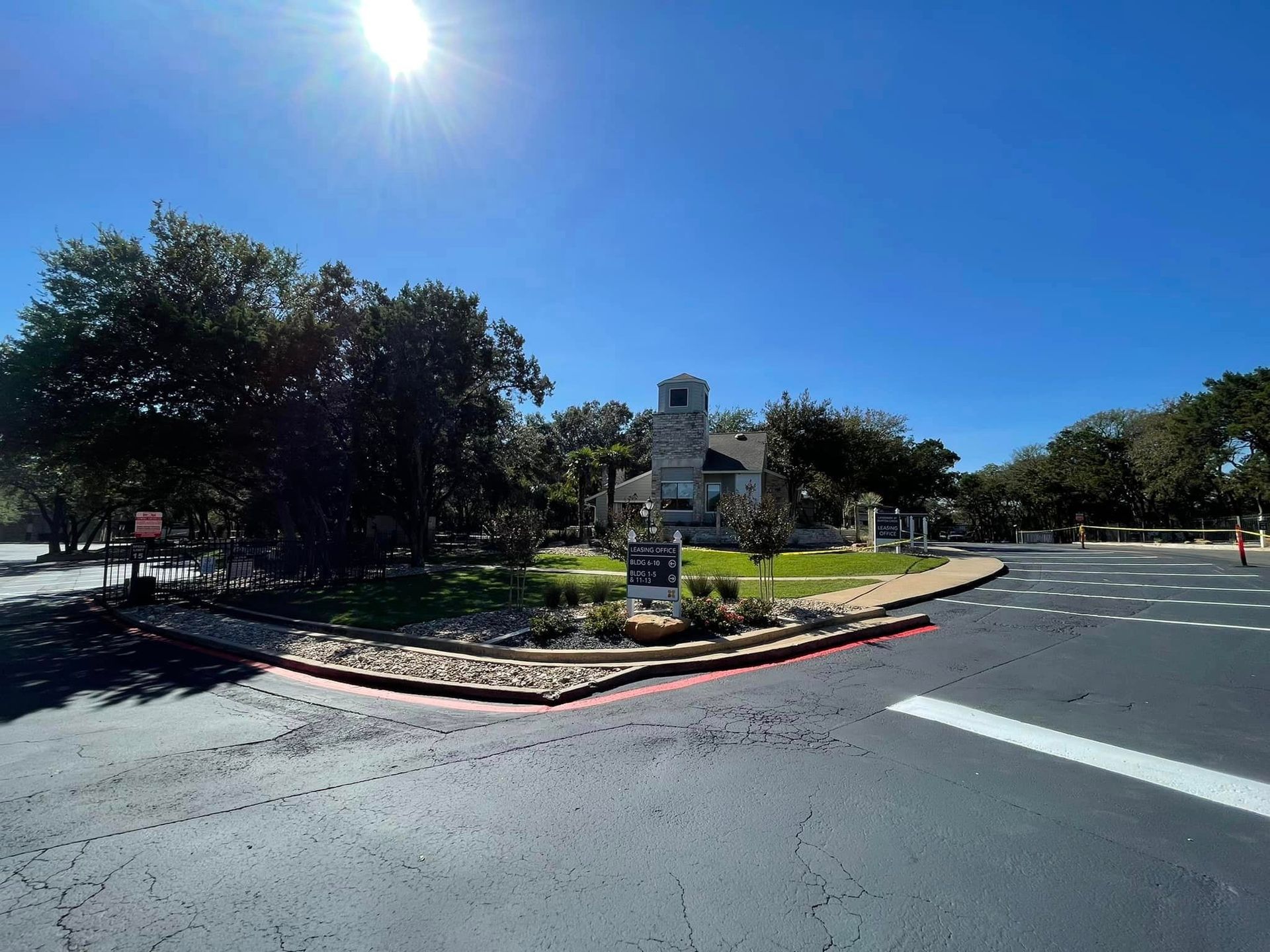 Entrance to a building with a tower, surrounded by trees and a circular drive on a sunny day.
