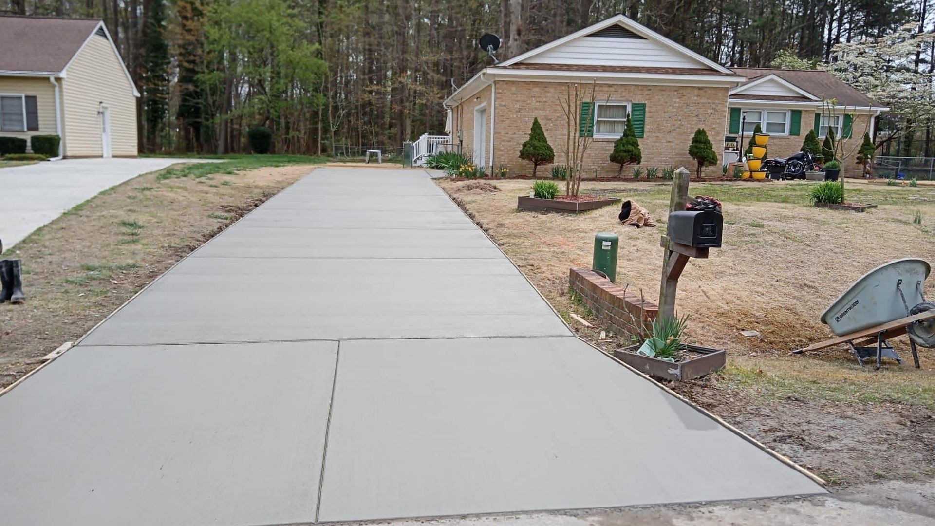 New concrete driveway leading to a brick house with a mailbox in the foreground.
