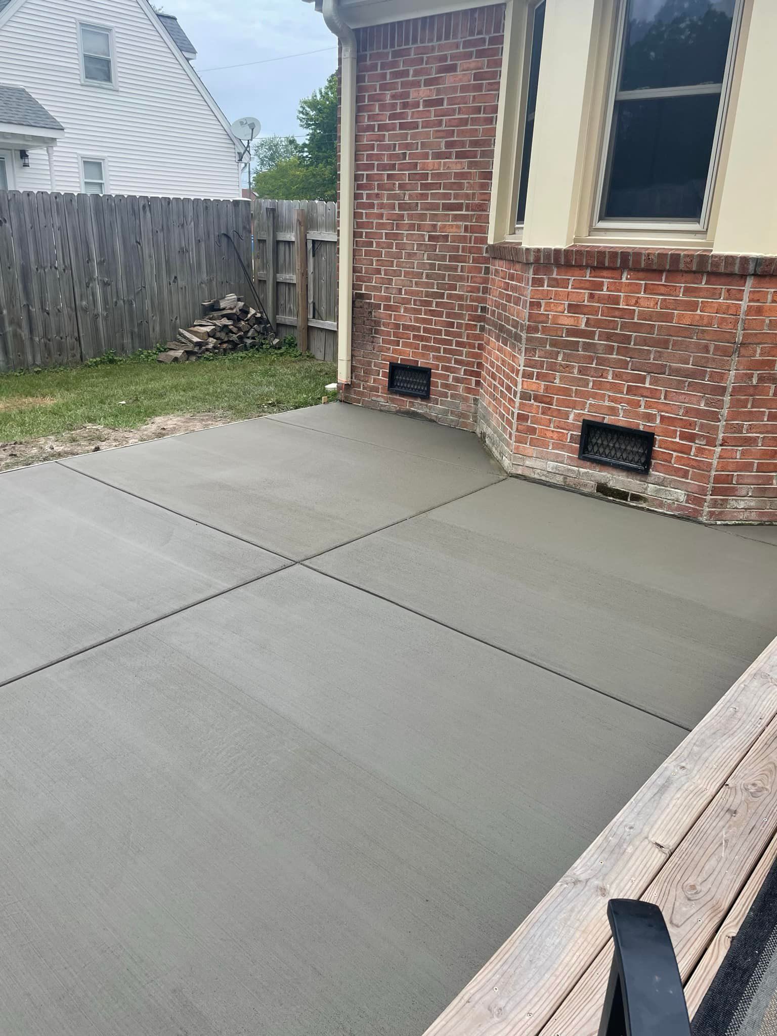 Gray concrete patio next to a brick house with a wooden fence and deck.