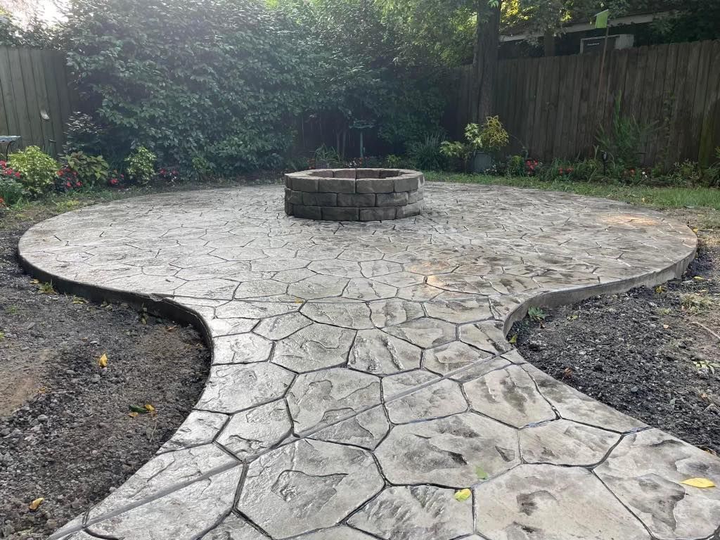 Concrete patio with a stone fire pit. A patterned walkway leads to the fire pit area.
