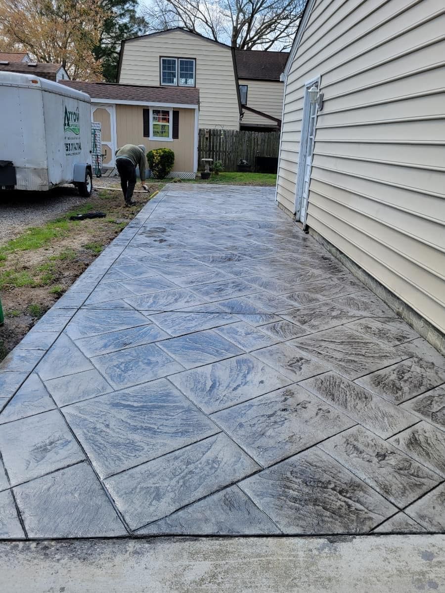 Stamped concrete patio with a person working near a house and trailer.
