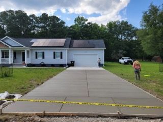 Newly poured concrete driveway in front of a light blue house with solar panels and people nearby.